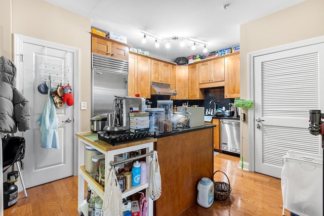 kitchen featuring light wood-style flooring, stainless steel appliances, under cabinet range hood, dark countertops, and tasteful backsplash