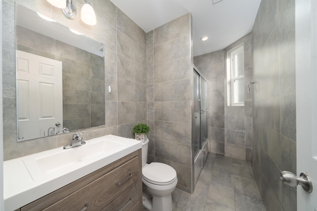 bathroom with tile walls, vanity, a shower with door, and toilet