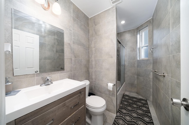 bathroom with a shower with shower door, tile patterned flooring, toilet, tile walls, and vanity