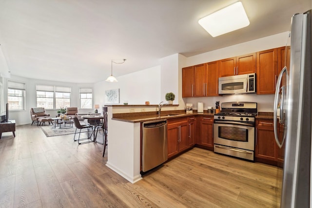 kitchen featuring a peninsula, appliances with stainless steel finishes, brown cabinetry, dark countertops, and decorative light fixtures