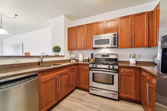 kitchen with decorative light fixtures, appliances with stainless steel finishes, light wood-style floors, a sink, and dark stone counters