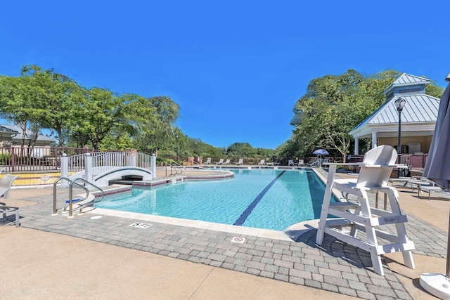 community pool with a patio area, a hot tub, and fence