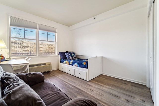 bedroom with a view of city, an AC wall unit, wood finished floors, and baseboards