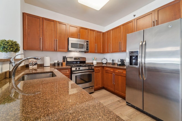 kitchen featuring brown cabinets, appliances with stainless steel finishes, dark stone counters, and a sink