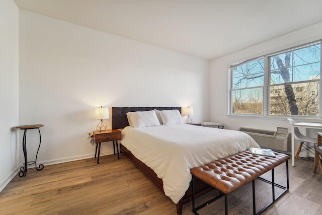 bedroom with baseboards, wood finished floors, and a wall mounted AC