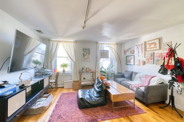 living room with light wood-type flooring, baseboard heating, and a healthy amount of sunlight