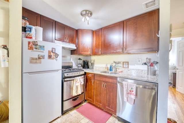 kitchen featuring appliances with stainless steel finishes, light stone counters, light hardwood / wood-style flooring, and sink