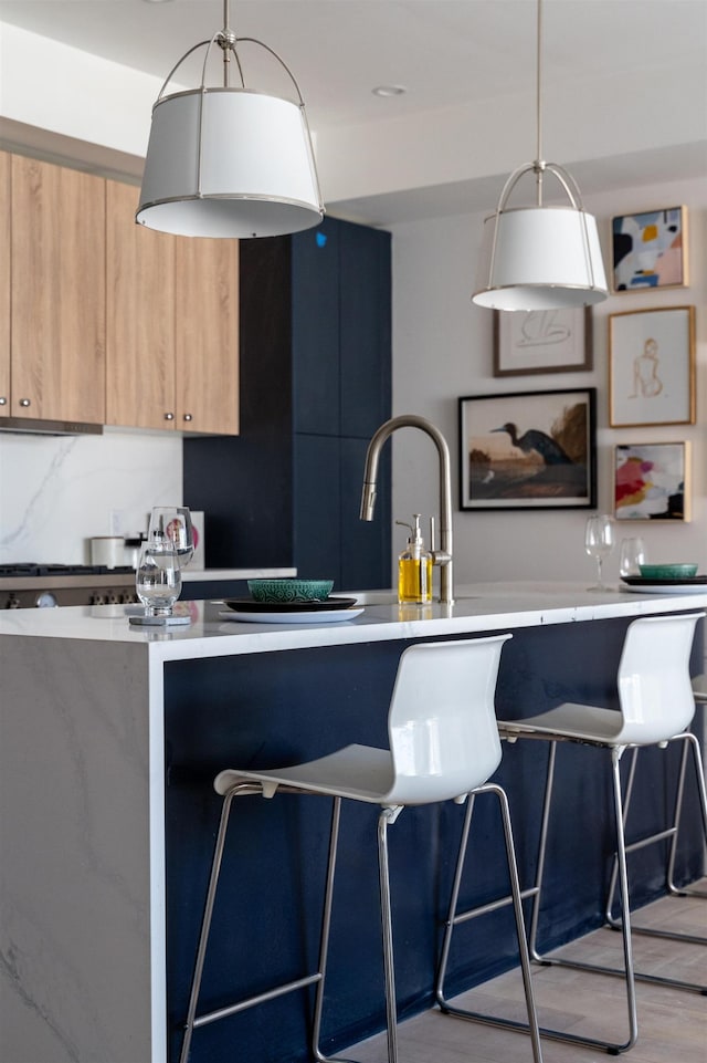 kitchen with modern cabinets, a breakfast bar area, hanging light fixtures, light countertops, and light brown cabinets