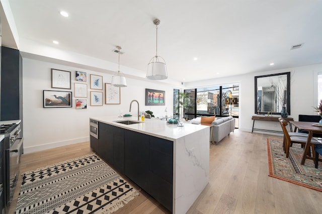 kitchen featuring light wood-style flooring, dark cabinets, a sink, light countertops, and stainless steel gas range