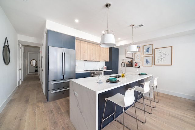 kitchen featuring light wood finished floors, modern cabinets, stainless steel refrigerator, a kitchen breakfast bar, and a sink