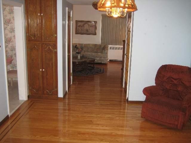 hallway featuring a notable chandelier, radiator heating unit, and light wood-type flooring