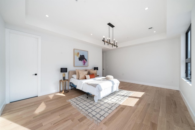 bedroom with a raised ceiling, light hardwood / wood-style floors, and a notable chandelier