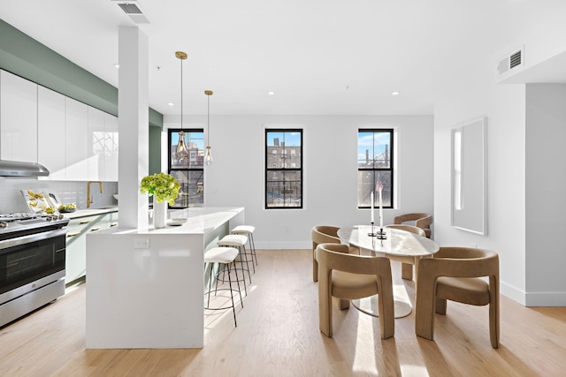 kitchen with white cabinets, stainless steel range oven, light wood-type flooring, hanging light fixtures, and a kitchen island