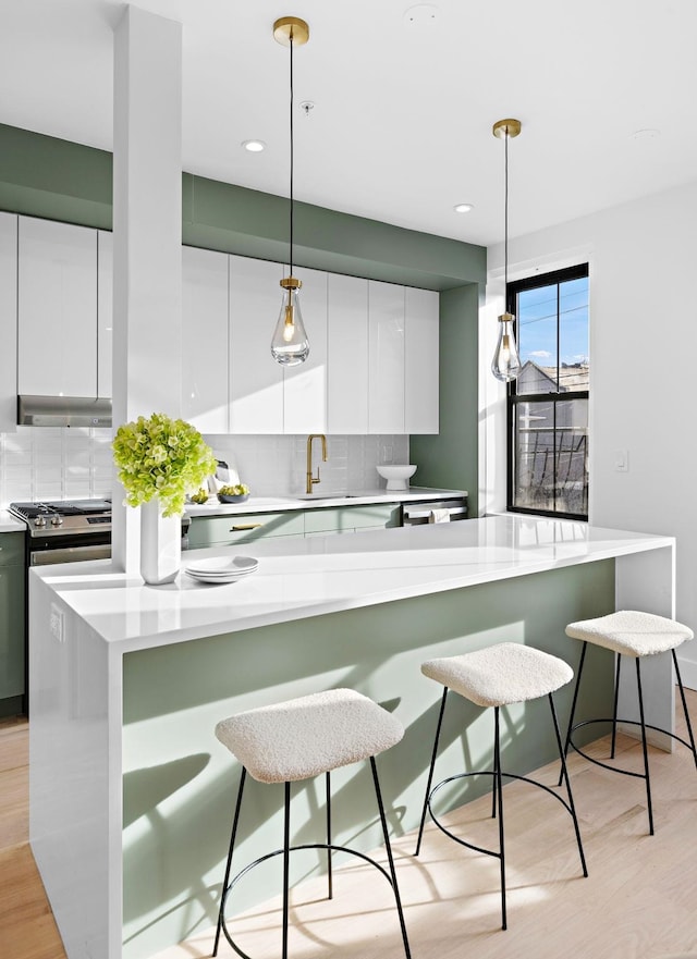 kitchen featuring extractor fan, white cabinets, a kitchen bar, and hanging light fixtures