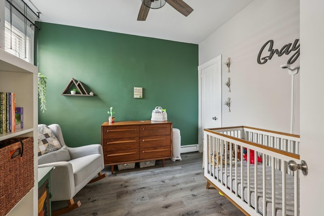 75 Poplar St, Jersey City, NJ 07307 - bedroom featuring a nursery area, wood finished floors, ceiling fan, and a baseboard radiator