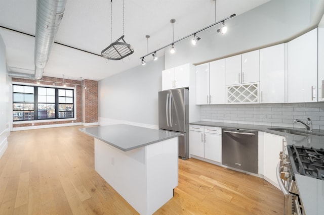 kitchen with light wood-style flooring, a sink, white cabinetry, appliances with stainless steel finishes, and brick wall