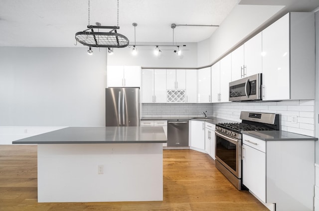 kitchen with light wood-style flooring, stainless steel appliances, dark countertops, tasteful backsplash, and a center island