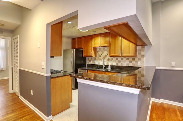 187 Wayne St Unit 208C, Jersey City, NJ 07302 - kitchen with freestanding refrigerator, a peninsula, dark stone counters, backsplash, and brown cabinets