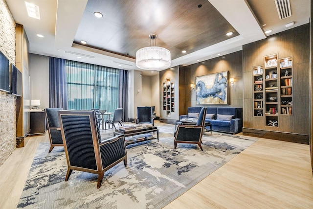 living room featuring built in features, light hardwood / wood-style flooring, and a raised ceiling