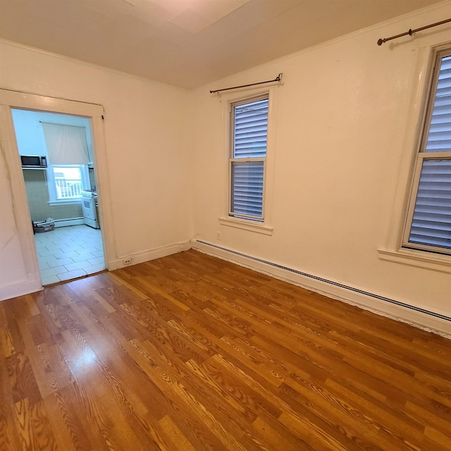 spare room featuring baseboard heating and wood-type flooring