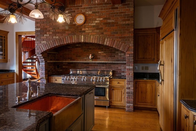 kitchen with range with two ovens, sink, dark stone countertops, and light wood-type flooring