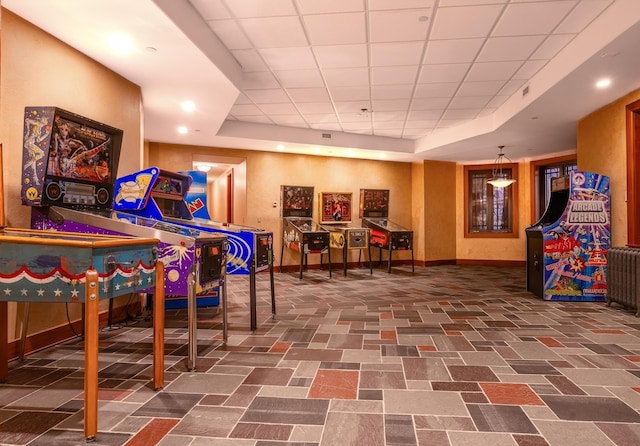 recreation room with a paneled ceiling, radiator, and a raised ceiling