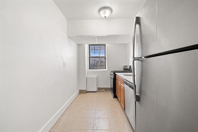 kitchen with light tile patterned floors, a drop ceiling, baseboards, appliances with stainless steel finishes, and brown cabinetry