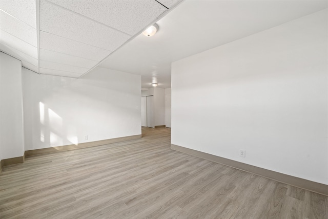 unfurnished room with light wood-type flooring, baseboards, and a paneled ceiling