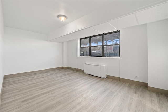 spare room with radiator, light wood-type flooring, and baseboards