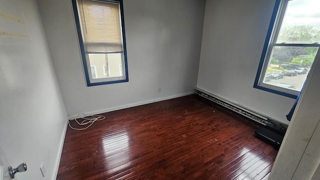 unfurnished room featuring a baseboard heating unit, a wealth of natural light, and dark hardwood / wood-style flooring