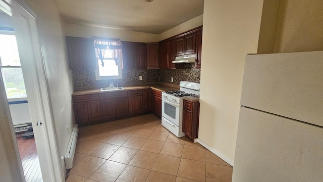 kitchen with sink, baseboard heating, light tile patterned floors, backsplash, and white appliances