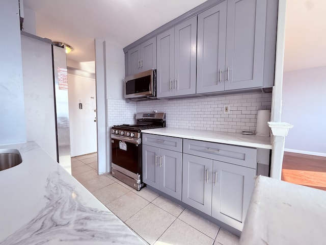 1225 Kennedy Blvd Unit 5E, Bayonne, NJ 07002 - kitchen featuring appliances with stainless steel finishes, gray cabinets, tasteful backsplash, light tile patterned floors, and light stone counters