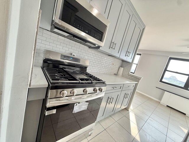 1225 Kennedy Blvd Unit 5E, Bayonne, NJ 07002 - kitchen with stainless steel appliances, gray cabinetry, tasteful backsplash, baseboards, and light stone counters