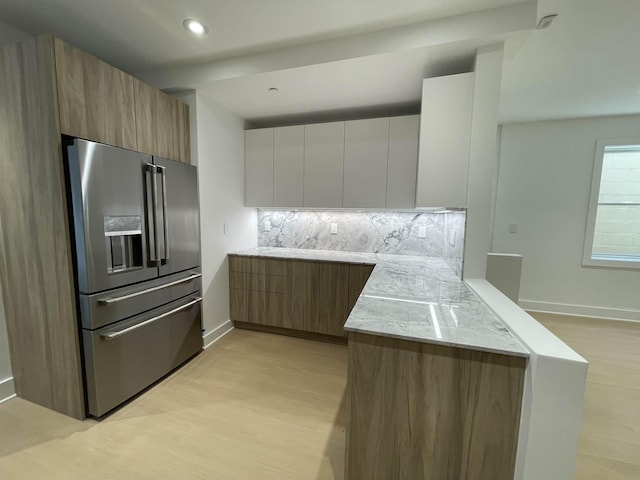 kitchen featuring kitchen peninsula, high end refrigerator, light wood-type flooring, tasteful backsplash, and white cabinets