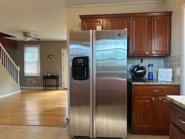 kitchen with light stone counters, ceiling fan, light hardwood / wood-style flooring, stainless steel fridge, and decorative backsplash