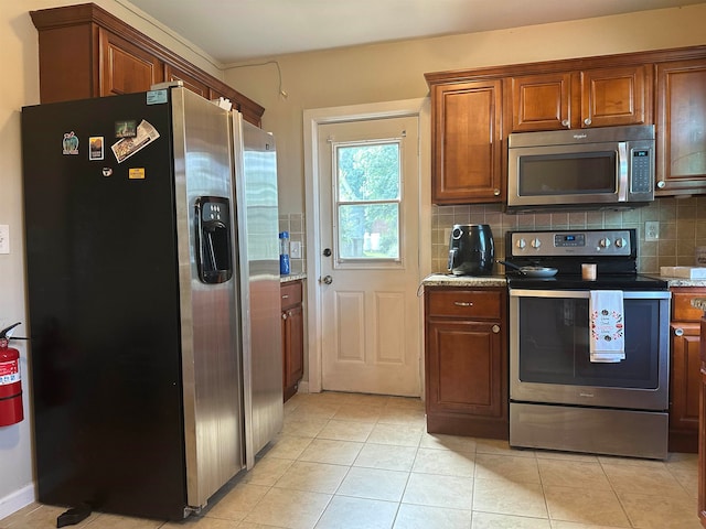 kitchen with appliances with stainless steel finishes, light tile patterned flooring, tasteful backsplash, and light stone countertops