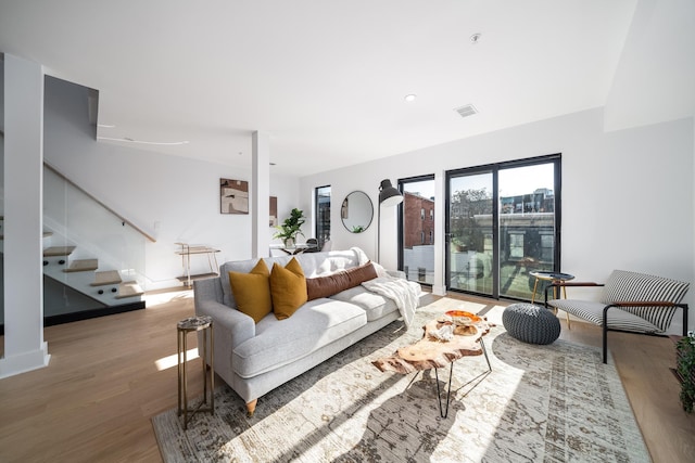 living room with stairs, visible vents, light wood-type flooring, and baseboards