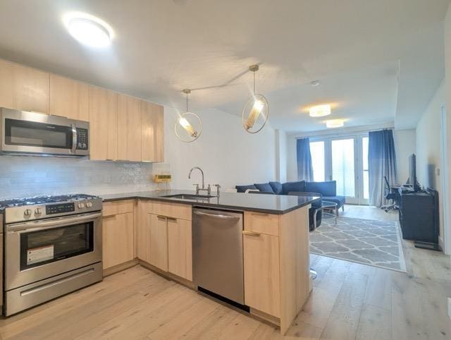 kitchen featuring light brown cabinets, stainless steel appliances, a peninsula, open floor plan, and hanging light fixtures