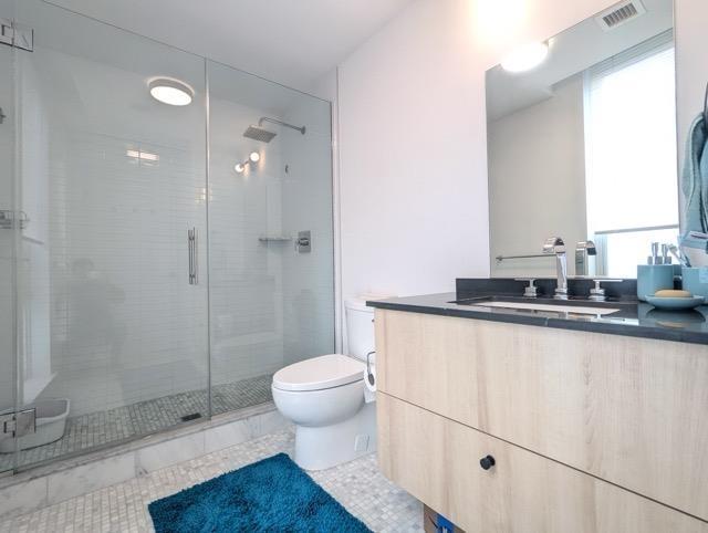 bathroom featuring tile patterned flooring, toilet, vanity, visible vents, and a shower stall