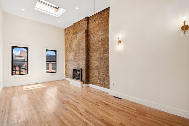 227 Bay St Unit 4B, Jersey City, NJ 07302 - unfurnished living room featuring a high ceiling, a skylight, a multi sided fireplace, light wood-type flooring, and brick wall