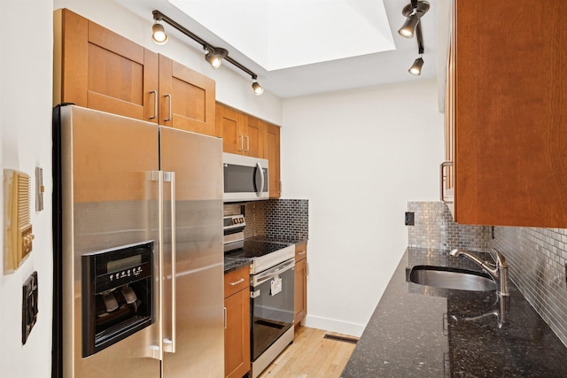 227 Bay St Unit 4B, Jersey City, NJ 07302 - kitchen with appliances with stainless steel finishes, rail lighting, dark stone counters, and brown cabinets