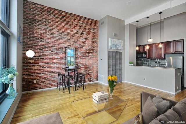 living area featuring brick wall, visible vents, a high ceiling, and wood finished floors