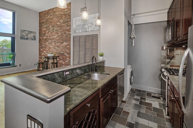 kitchen with a sink, baseboards, a peninsula, washer / dryer, and stainless steel appliances