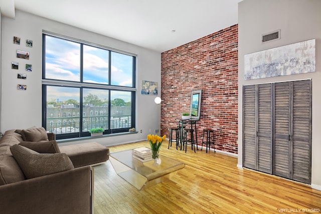 living area with visible vents, a high ceiling, brick wall, and wood finished floors