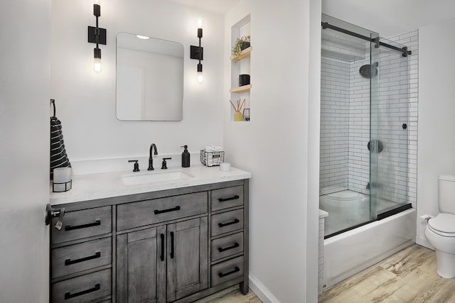 full bathroom featuring toilet, wood finished floors, shower / bath combination with glass door, and vanity