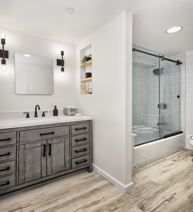 full bathroom with baseboards, combined bath / shower with glass door, wood finished floors, and vanity