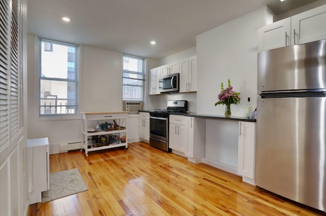 kitchen featuring stainless steel appliances, white cabinetry, baseboard heating, and a healthy amount of sunlight