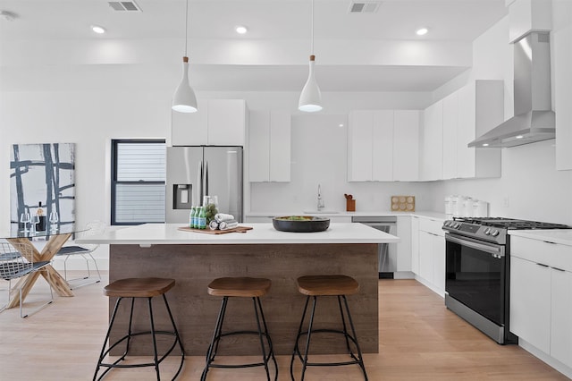 kitchen featuring stainless steel appliances, wall chimney range hood, white cabinetry, and a center island