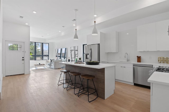 kitchen featuring a kitchen island, stainless steel appliances, pendant lighting, and white cabinetry