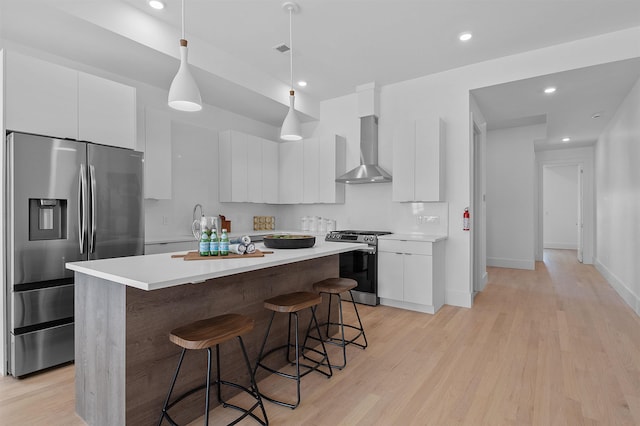 kitchen featuring stainless steel appliances, hanging light fixtures, a center island, wall chimney exhaust hood, and white cabinetry